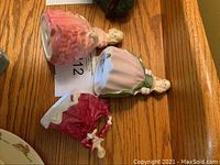 Three Royal Doulton figurines laid on wooden surface, view of bases and entire figures