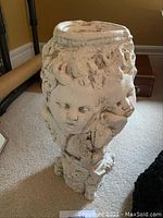 Full view of white sculpted pillar candle holder with faces and ornate classical decoration, showing form and texture.