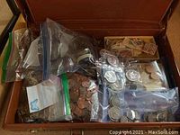 Open suitcase containing zipped bags and containers of mixed coins and stamps