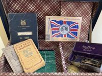 Photo showing the open trunk lined with plaid fabric containing several booklets including a 1952 calendar, Seaman discharge papers, Coronation 1953 postcard, and an Auto Strop safety razor box with accessories.