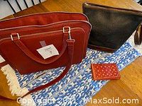 New red Danier leather briefcase, black Roots shoulder bag, and small red wallet shown on table.