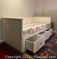 White wooden IKEA single bed with three large storage drawers pulled out and mattress on top.