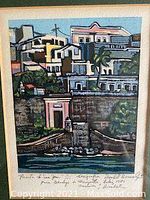Close-up of framed serigraphic print named 'Puerto de San Juan', showing colorful coastal buildings near water, signed and numbered.