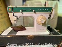 Singer sewing machine on top of its original carrying case featuring white and green body and sewing needle area with fabric placed under needle