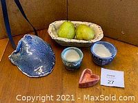 Various handmade ceramic pieces including a blue shell dish, rectangular patterned bowl, two small round bowls, and a red heart dish. One bowl contains pears, other bowls have salt or similar substances.