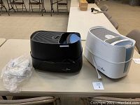 Two Germ Free humidifiers, one black and one white, side by side on a table with power cords.