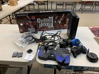Photo of the entire lot showing Sony PS2 console, multiple controllers including a MadCatz joystick and Pelican wireless controller, memory cards, extension cables, and Guitar Hero guitar with game in its box.