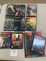 9 PlayStation 2 superhero and action game cases along with Spiderman Official Strategy Guide laid flat on a white surface.