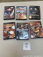 Photo showing six PlayStation 2 game cases arranged in a grid on a carpet surface with a MaxSold lot number card 12.