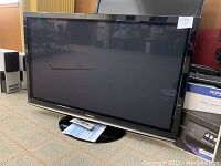 Front view of the black Panasonic Viera 50-inch TV on its pedestal stand, with papers and a remote underneath.