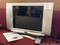 Front view of Syntax Olevia 20-inch LCD TV with remote and user manual placed beside it on a couch.