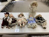 Set of six porcelain dolls on a table, two sharing a swing, one with own swing, detailed vintage clothing, some wear visible.
