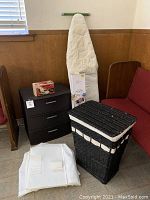 Full view of storage drawer, ironing board, vintage Easy Iron box on top, and woven laundry hamper.