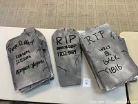 Three gray styrofoam Halloween headstones with black inscriptions and crack detailing