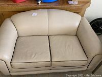 Front view of beige loveseat showing two seat cushions with dark piping, rounded armrests, and curved backrest.