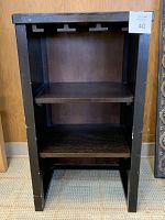 Front view of wooden bar cabinet showing three shelves and wineglass racks on the upper section. Dark stained wood with minor scuffs on legs and slight bubbling on top surface.