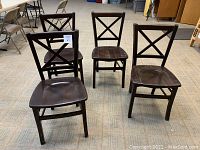 Four wooden dining chairs with dark finish grouped and spaced apart, showing overall condition and design.