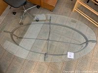 Top view of oval metal and glass coffee table showing clear glass top and metal frame, including a visible smudge or mark on the glass surface.