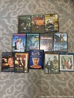 Photo of 12 assorted DVD movie cases laid out on carpet, titles visible to identify movies included in the lot.