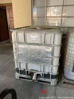 Front and side view of a large rectangular water storage container enclosed in a metal cage frame with a spigot on the front near the base.
