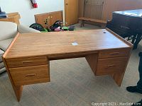 Full wooden desk showing five drawers, flat top surface, and leg openings.