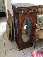 Front and side view of ornate wooden display cabinet with oval glass window and carved details.
