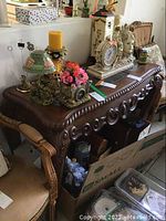 Side view of carved wooden entry table with decorative items on top and boxes underneath.