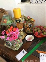 Photo showing multiple decorative items including floral cart, candle holder with yellow candle, floral photo frame, a small floral dish, and a red bowl with faux strawberries