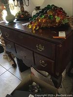 Front view of the wood buffet showing four drawers with ornate brass handles and polished finish, objects on top not included.