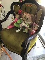 Front and angle views of the dark wood side chair upholstered in green velvet filled with assorted stuffed animals and a floral pillow.