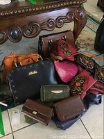 Overview of assorted bags and purses including black tote with gold studs, orange handbag, red purses with floral designs, and brown wallets.