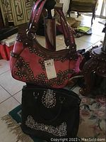 Two bags: pinkish-brown Montana West purse with dark brown studded trim and details in western style, and a black Montana West rolling bag with white embroidery and stud accents.