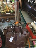 Two brown Montana West bags, a rolling travel bag with retractable handle and matching purse, both with studded tooled leather design