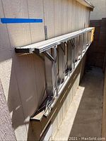 Side view of the 8-foot aluminum ladder leaning against the outdoor wall showing the length and overall structure.