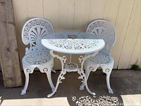 Front view of white wrought iron round table with two matching ornate chairs.
