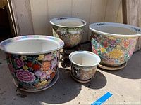 Overall view of five Japanese ceramic planters with floral and traditional designs arranged together, showing various sizes, colors, and patterns.
