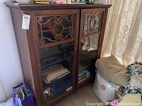 Front angled view showing both glass doors with decorative wood paneling, dark wood finish, and items stored inside.