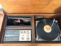Open top view of the console showing the functional components inside including the record player turntable with vinyl record, and the AM/FM radio control panel with dials and tuning meters.