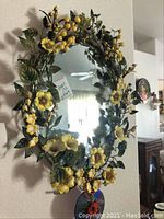 Front view of oval floral metal mirror with yellow flowers, green leaves, and decorative berries.