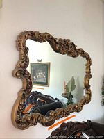 Front view of ornate rectangular wall mirror with gold-tone carved frame showing decorative scroll and leaf motifs