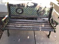 Front view of outdoor wooden bench with green metal frame and lattice backrest with round decorative elements. Weathered wood slats on seat and backrest.