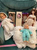 View showing collection of dolls seated and standing on green chair including baby doll and plush throw