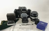 Overview of Nikon FTN camera body with NIKKOR-S 50mm lens, Schneider Kreuznach lens in box, two waist-level viewfinders, pouches and guarantee certificate