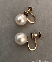 Pair of 18K gold screw-on earrings with creamy South Sea pearls, approximately 1 cm each, lying side by side on gray background.