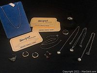 Multiple gold jewelry pieces including rings, earrings, pendants, necklaces and two Add-a-Pearl cards displayed on black surface