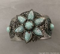 Front view of the cuff showing the large turquoise-colored flower on mesh medallion and surrounding decorative metal band.