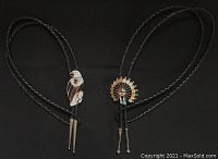 Two smaller Zuni bolo ties with braided leather ties and metal aiguillettes against black background
