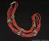 Full view of multi-strand coral and silver necklace on black background