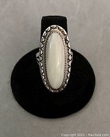 Front view showing the elongated creamy oval stone set in a toothed sterling silver bezel with hand-stamped border.