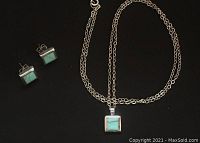 Photo showing the turquoise and sterling silver stud earrings and matching pendant on chain against a black background.
